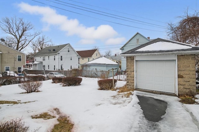 snowy yard with a garage, an outbuilding, and fence