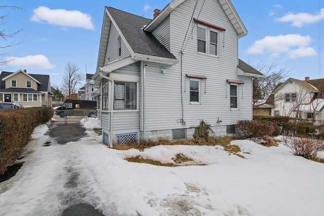 view of snowy exterior featuring a shingled roof, a chimney, and a residential view