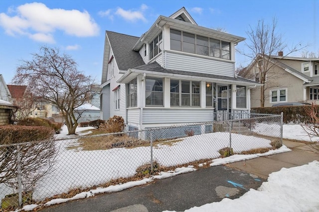 view of front of house featuring a sunroom, a fenced front yard, and roof with shingles