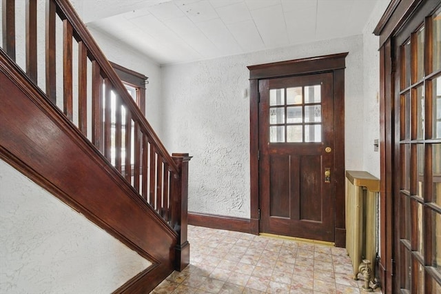 entryway featuring light floors, a textured wall, stairway, and baseboards