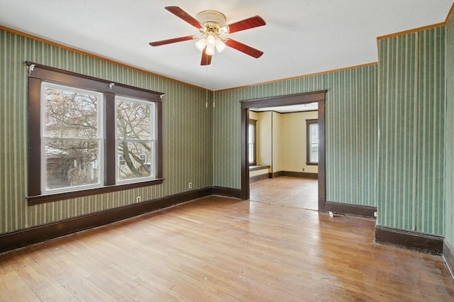 empty room with light wood finished floors, ceiling fan, baseboards, and wallpapered walls