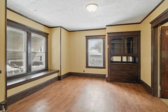 unfurnished room with ornamental molding, a textured ceiling, baseboards, and wood finished floors