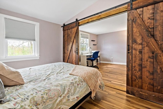 bedroom with baseboards, vaulted ceiling, a barn door, and wood finished floors