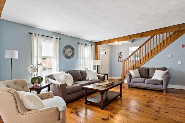 living room featuring baseboards, light wood-type flooring, beam ceiling, and stairs