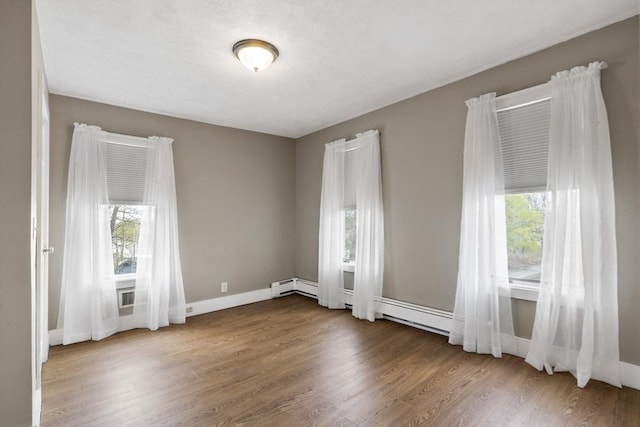 spare room featuring baseboards, a baseboard radiator, wood finished floors, and a wealth of natural light