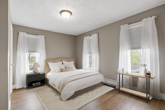 bedroom with baseboards, a baseboard radiator, wood finished floors, and multiple windows