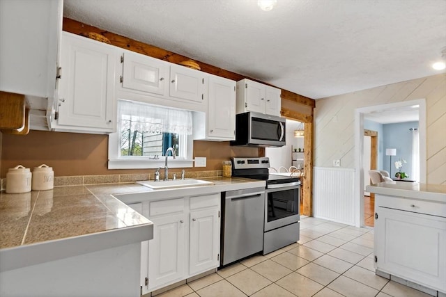 kitchen with a sink, tile counters, wood walls, stainless steel appliances, and white cabinetry