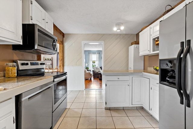 kitchen featuring a textured ceiling, wood walls, stainless steel appliances, white cabinetry, and light tile patterned floors
