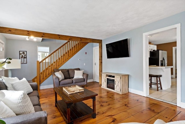 living room featuring baseboards, light wood-type flooring, stairs, and beam ceiling