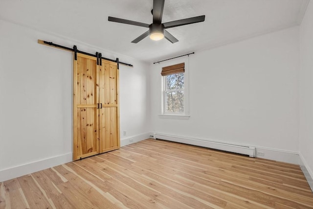 empty room with a baseboard heating unit, a barn door, baseboards, and light wood-style floors