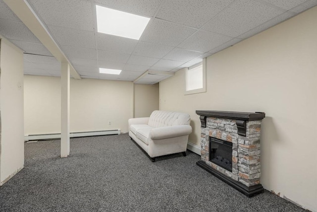 living area featuring baseboard heating, carpet flooring, a stone fireplace, and a drop ceiling