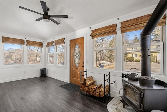 sunroom / solarium featuring vaulted ceiling, ceiling fan, plenty of natural light, and a wood stove