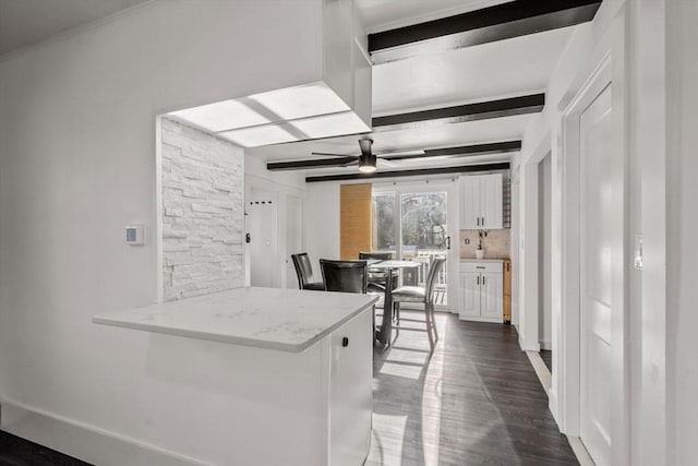 kitchen with decorative backsplash, a ceiling fan, white cabinets, light stone countertops, and beam ceiling