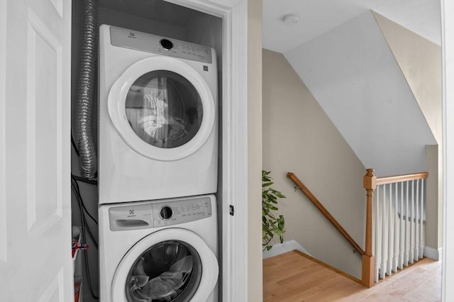 laundry area with baseboards, stacked washing maching and dryer, and wood finished floors