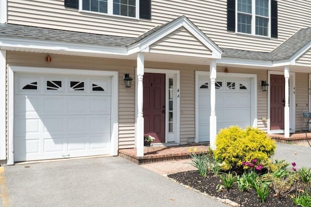 property entrance with a porch, an attached garage, driveway, and roof with shingles