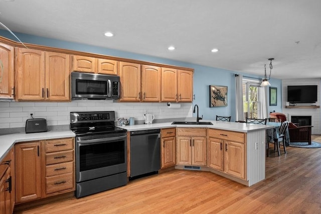 kitchen with decorative backsplash, a peninsula, light wood-type flooring, a sink, and stainless steel appliances