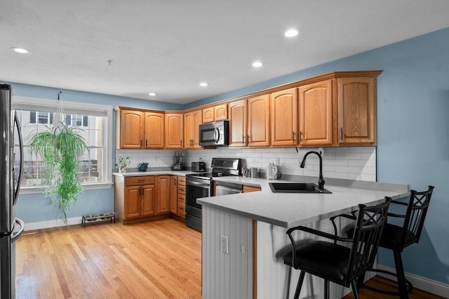 kitchen with appliances with stainless steel finishes, a sink, a peninsula, baseboards, and decorative backsplash