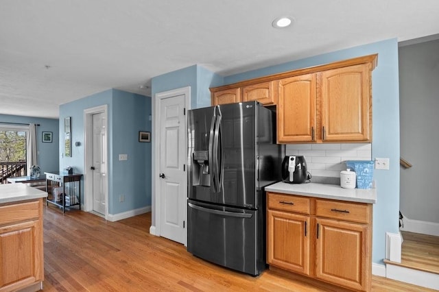 kitchen featuring baseboards, light wood finished floors, black refrigerator with ice dispenser, and tasteful backsplash