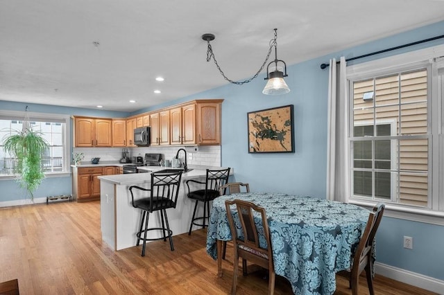 kitchen featuring a kitchen breakfast bar, backsplash, light wood-type flooring, a peninsula, and electric stove