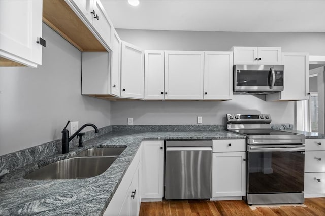 kitchen with appliances with stainless steel finishes, white cabinetry, dark wood-type flooring, and a sink