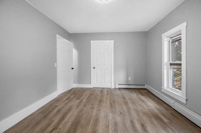 empty room featuring wood finished floors, baseboards, and a baseboard radiator