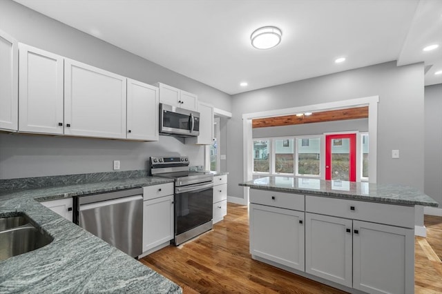 kitchen with recessed lighting, dark stone countertops, stainless steel appliances, and wood finished floors