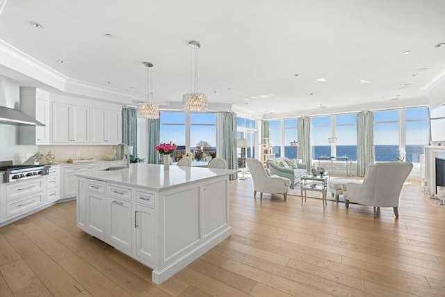 kitchen featuring a water view, decorative light fixtures, light hardwood / wood-style flooring, a kitchen island with sink, and white cabinets