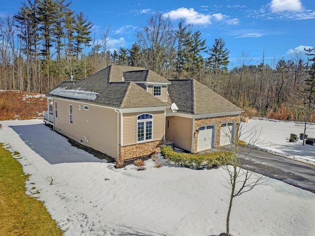 view of front of property with a garage, stone siding, roof with shingles, and driveway