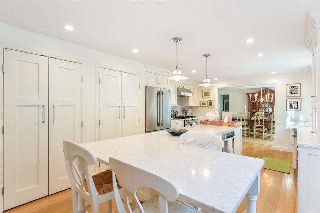 kitchen with white cabinetry, a large island, hanging light fixtures, light hardwood / wood-style floors, and appliances with stainless steel finishes