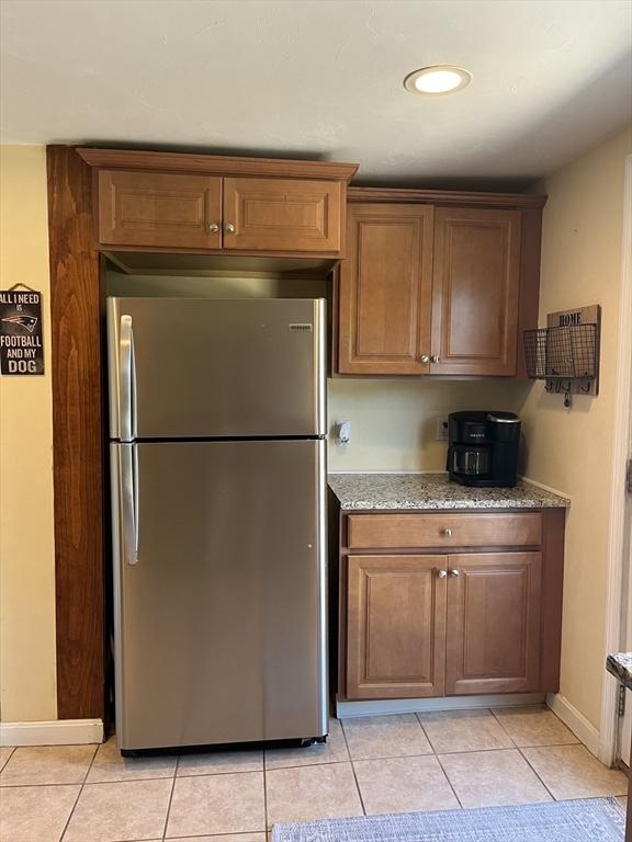 13 Harrison Ave, Bourne, MA 02532 - kitchen with freestanding refrigerator, light tile patterned floors, light stone counters, and brown cabinetry