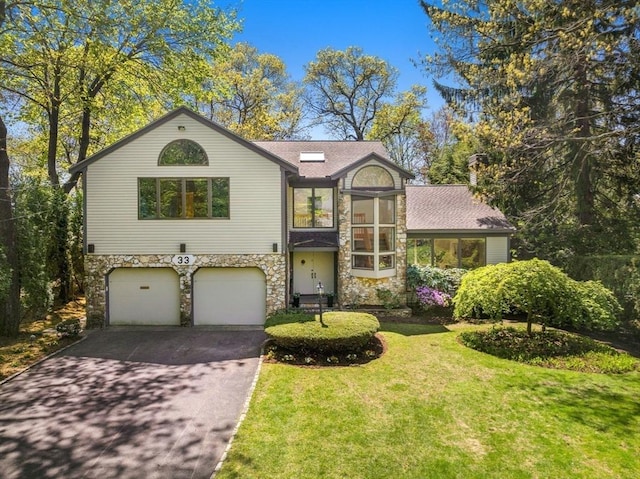 view of front of house featuring an attached garage, driveway, stone siding, and a front lawn