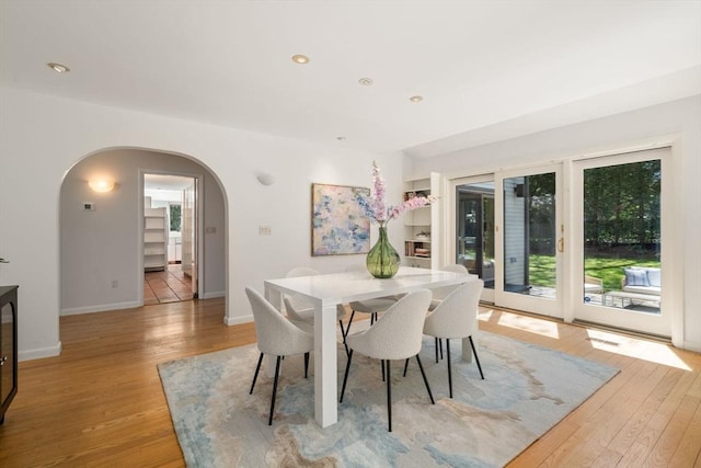 dining area with arched walkways, baseboards, recessed lighting, and light wood-style floors