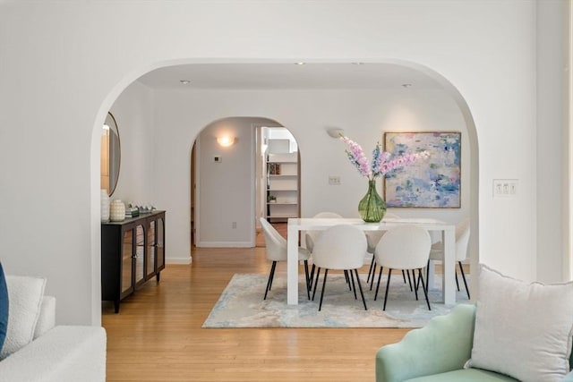 dining room featuring arched walkways, baseboards, and light wood-type flooring