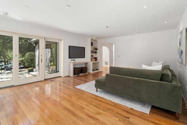 living room featuring light wood-style floors, arched walkways, recessed lighting, and built in shelves