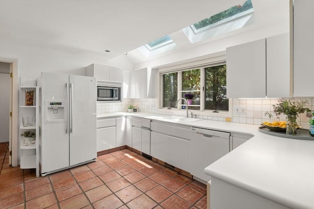 kitchen with decorative backsplash, white appliances, lofted ceiling with skylight, white cabinets, and a sink