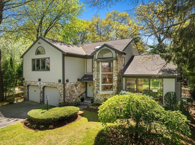 view of front facade with roof with shingles, stone siding, a garage, a front yard, and driveway