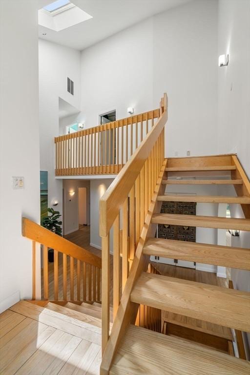 staircase with a skylight, a towering ceiling, wood finished floors, and visible vents