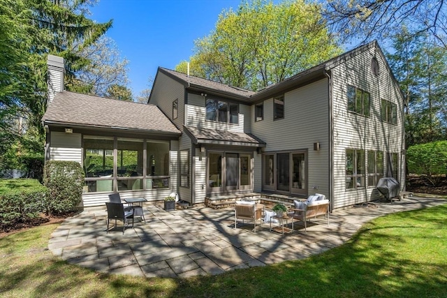 back of property with a shingled roof, a chimney, an outdoor living space, a patio, and a yard