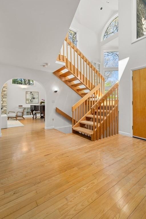 interior space featuring wood-type flooring, arched walkways, high vaulted ceiling, stairs, and baseboards