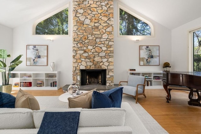 living area with high vaulted ceiling, a stone fireplace, and wood finished floors