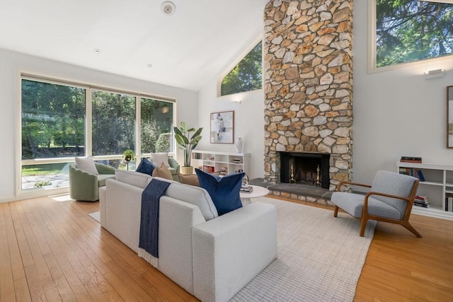 living room featuring high vaulted ceiling, a fireplace, and light wood-style flooring