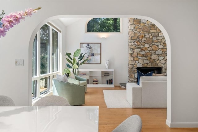 living room featuring a stone fireplace, arched walkways, wood finished floors, baseboards, and lofted ceiling