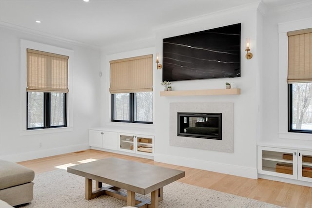 living area featuring plenty of natural light, ornamental molding, wood finished floors, and a glass covered fireplace