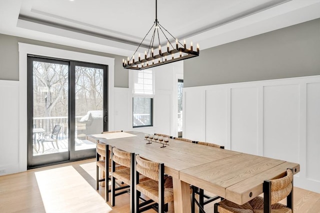 dining area with a wainscoted wall, light wood-style flooring, a tray ceiling, and a decorative wall