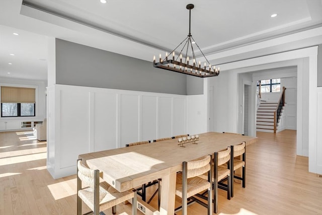 dining room with a raised ceiling, a wainscoted wall, light wood-style flooring, stairs, and recessed lighting