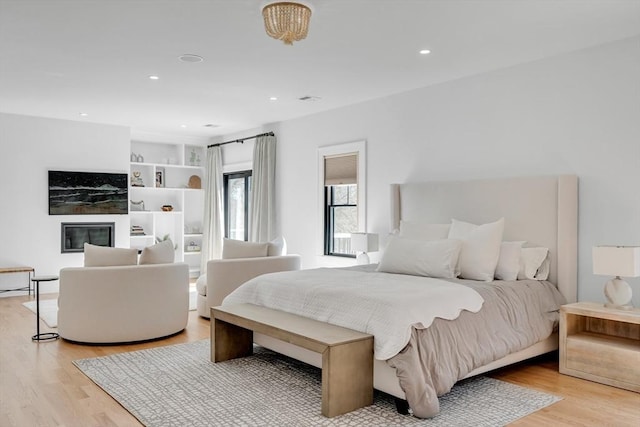 bedroom with light wood-type flooring, visible vents, a glass covered fireplace, and recessed lighting