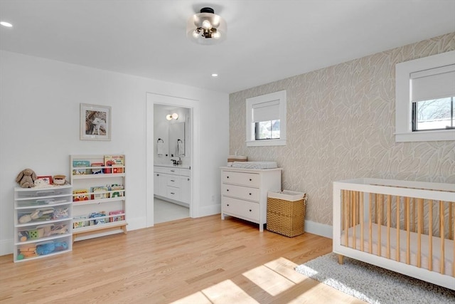 bedroom featuring recessed lighting, wood finished floors, baseboards, a crib, and wallpapered walls