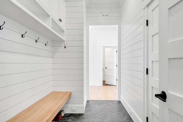 mudroom with crown molding, wooden walls, and baseboards