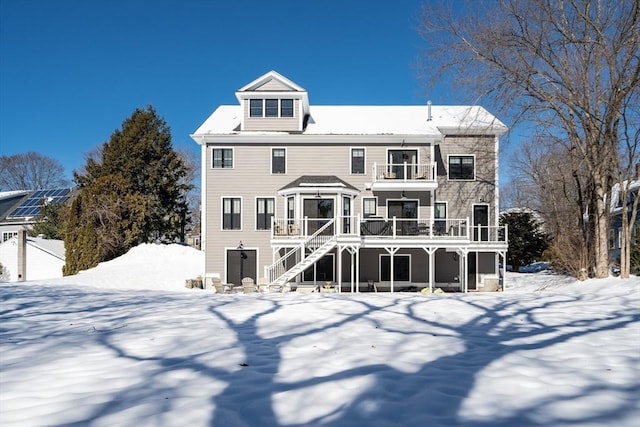 snow covered house featuring a balcony and stairway