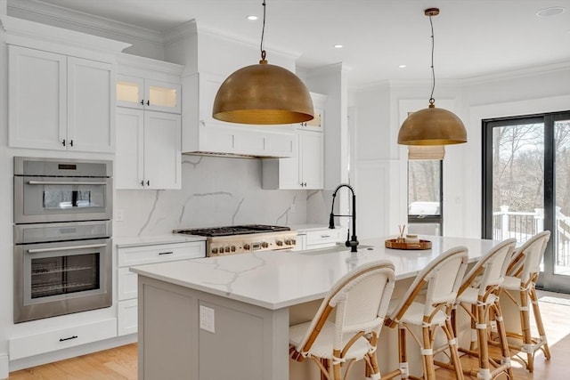 kitchen with stainless steel appliances, white cabinetry, decorative backsplash, a center island with sink, and crown molding